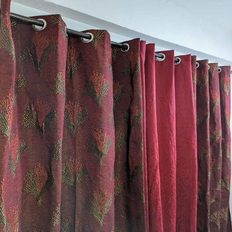 Red curtains with a leaf pattern hanging from a rod against a white wall.
