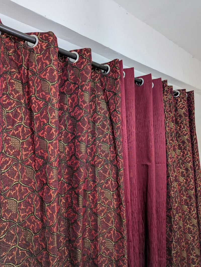 Red patterned curtains hanging from a rod against a white wall.